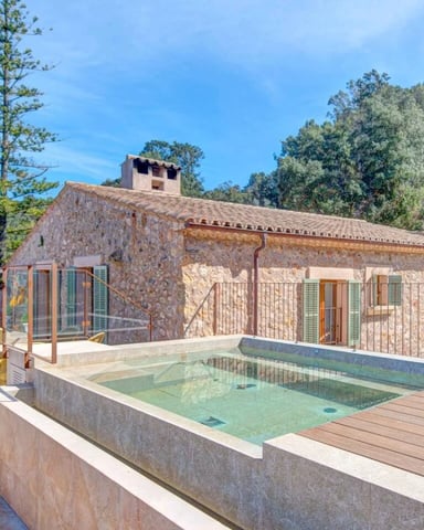 Stone villa with pool and wooden deck surrounded by pine trees and green shutters