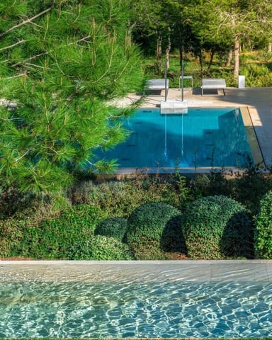 Modern pool terrace with turquoise water, white pergola, manicured hedges, and forested hillside beyond