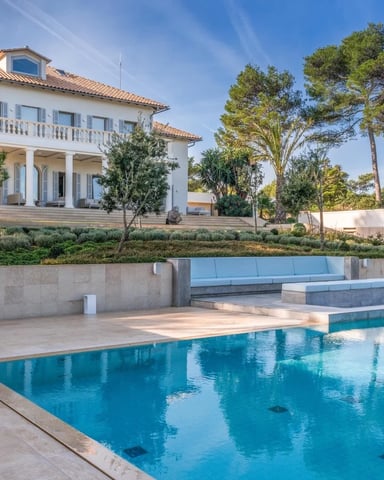 Mediterranean villa with terracotta roof, white facade, and swimming pool surrounded by stone patio and pine trees