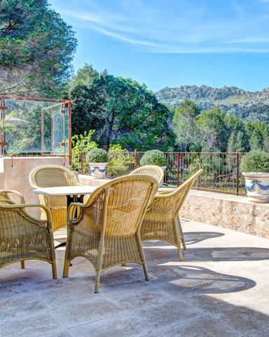 Terrace with wicker chairs and table overlooking forested mountains and rocky hills under clear blue sky