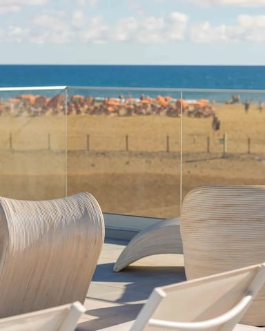 Modern curved white chairs on a rooftop terrace overlooking a sandy beach with ocean and blue sky