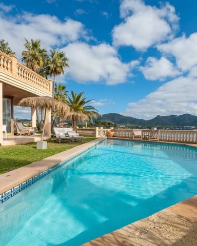 Luxury villa with swimming pool, manicured lawn, stone terrace, and mountain views under clear blue sky