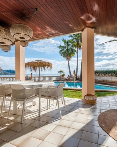 Covered terrace with woven pendant lights, dining table, pool, and bay view with palm trees and mountains