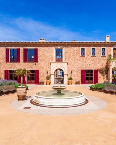 Terracotta villa with red shutters, central courtyard fountain, lavender gardens, and wooden benches under blue sky