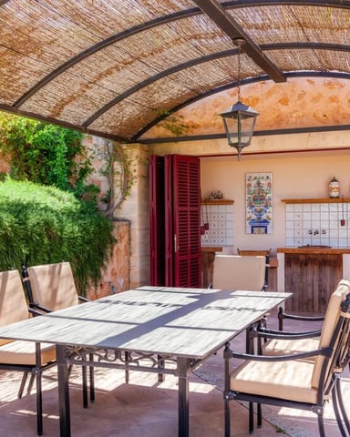 Covered patio with dining table, chairs, climbing vines, and kitchenette with tiled backsplash