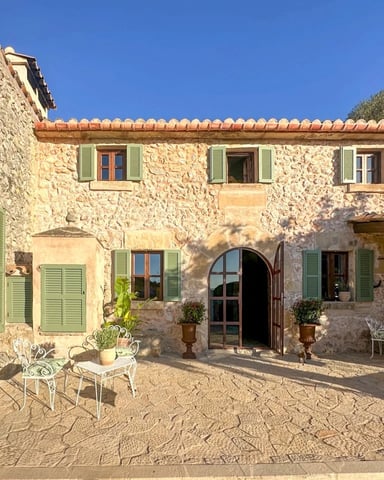 Tuscan stone villa with green shutters, arched doorway, and courtyard with wrought-iron seating