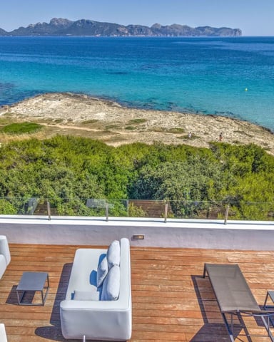 Wooden deck with lounge chairs and seating overlooking turquoise Mediterranean sea, rocky coastline, and distant mountains