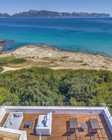 Modern terrace with wooden deck overlooking turquoise Mediterranean bay, rocky coastline, and distant mountains