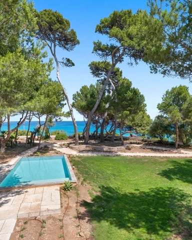 Beachfront property with swimming pool, lounge chairs, manicured lawn, pine trees, and turquoise Mediterranean Sea view