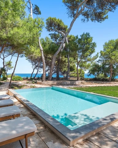 Swimming pool with loungers overlooking Mediterranean Sea and pine trees, clear blue sky