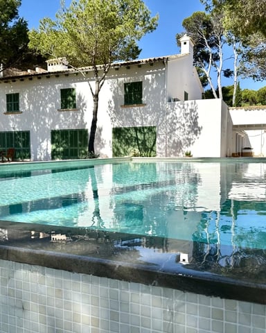 White Mediterranean villa with green shutters and turquoise swimming pool surrounded by mature trees