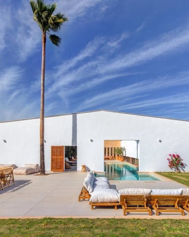 Modern white villa with pool, wooden loungers, palm tree, and manicured grounds under blue sky