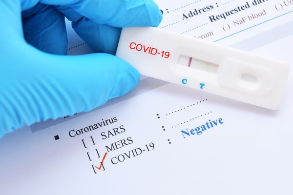 Gloved hands holding COVID-19 test result form showing negative result