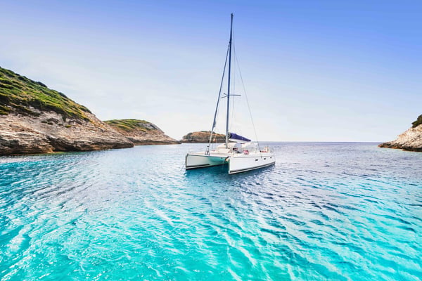 White sailboat anchored in turquoise water between rocky cliffs under clear blue sky