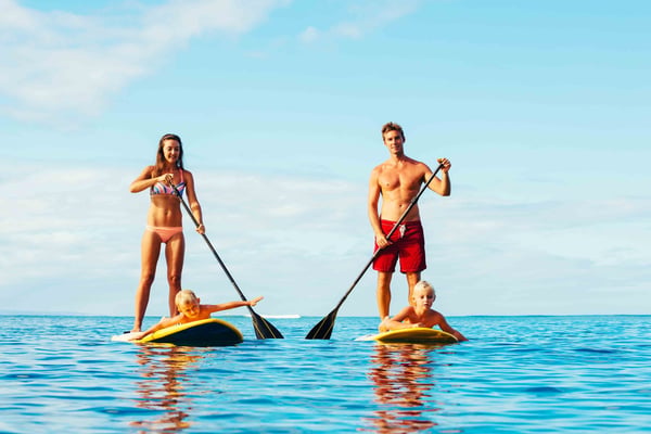 Family paddleboarding in clear blue ocean water on a sunny day